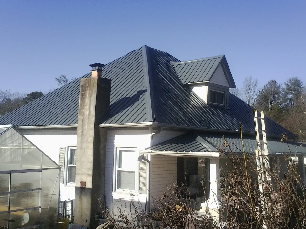 Dark blue standing seam metal roof on a white farmhouse with dormer — Slate & Tile Roof Repair by Roofing Brothers in Maple