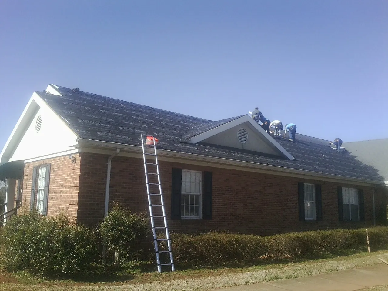 Crew tearing shingles off a brick ranch roof with a ladder set — Emergency Roof Repair work by our crew in Maple