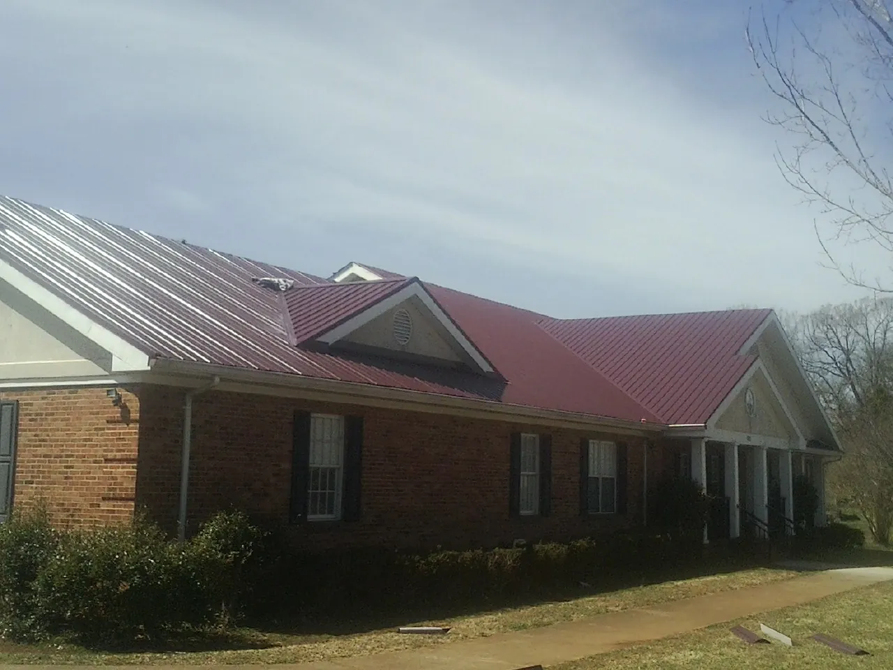 Red metal roof with gabled entries on a long brick building, from a Hail Damage Roof Repair job in Maple