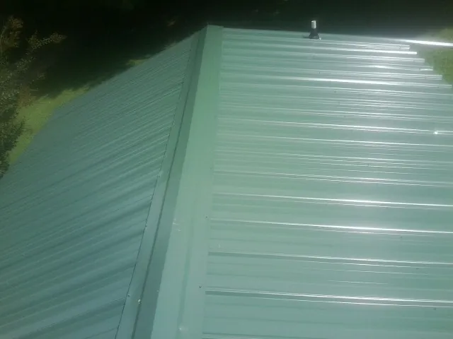 New green metal panels meeting at the ridge of a roof — Flat Roof Repair work by our crew in Maple