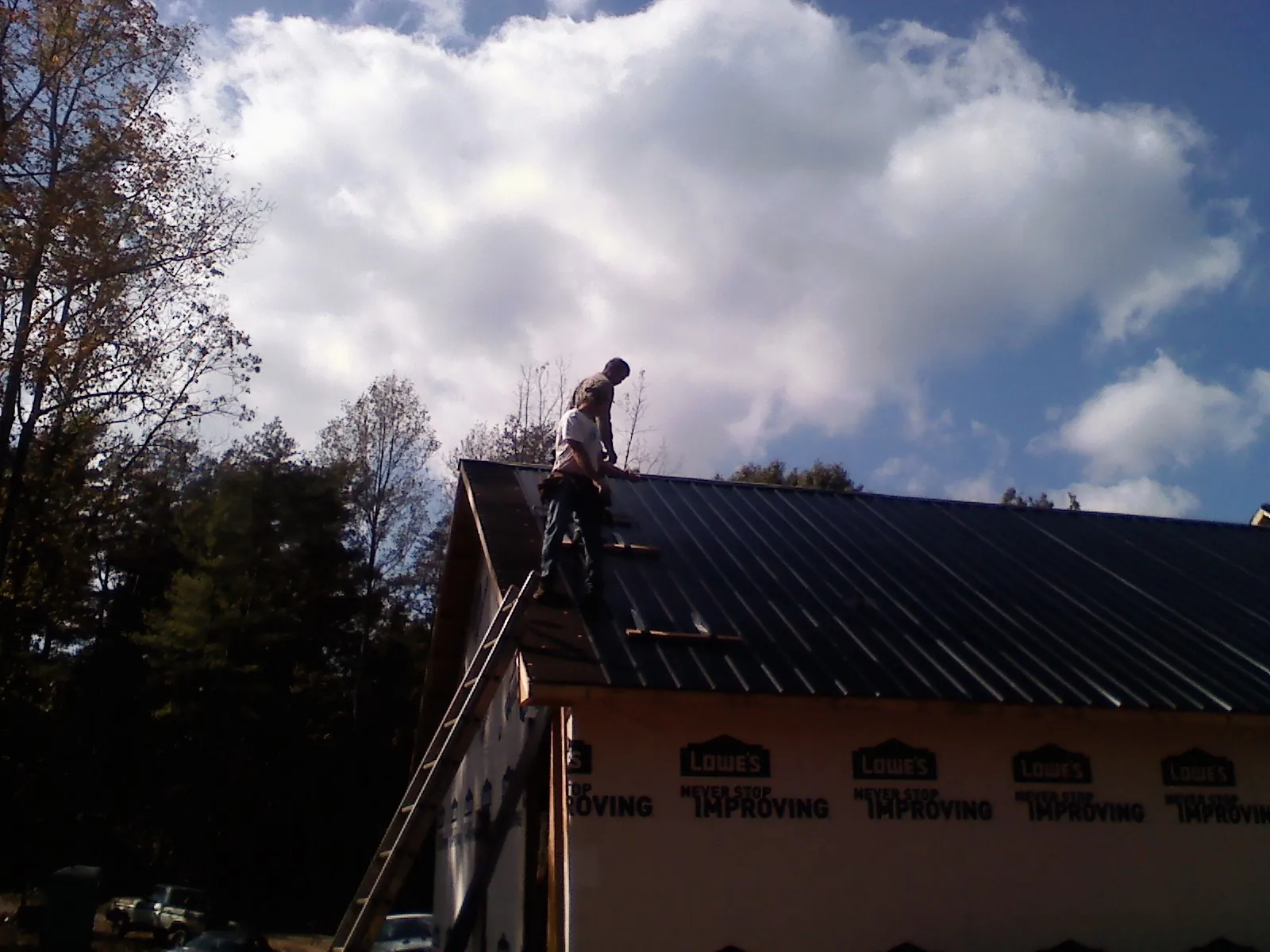 Roofer fastening dark metal panels high against a cloudy sky, from a Roof Inspection job in Maple